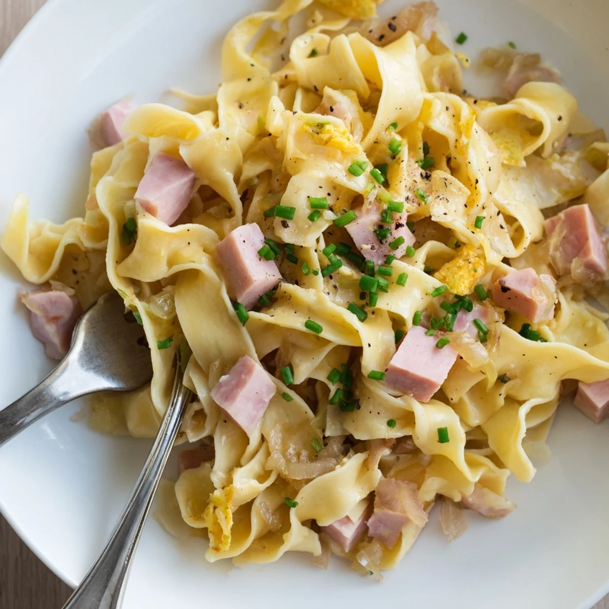 Zarte Eiernudeln mit würzigem Schinken, Zwiebeln und frischen Kräutern vereint.  