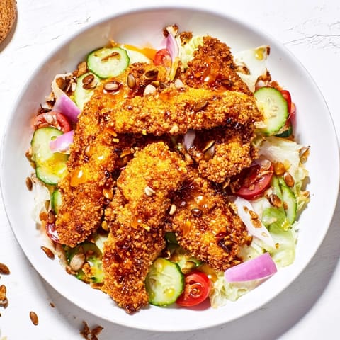 Crispy Hot Honey Chicken Salad mit goldbraunen Streifen und frisch gemischtem Römersalat auf einem Holztisch.