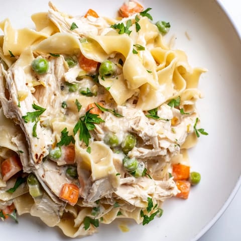 Goldbraune Nudeln in cremiger Sauce mit zartem Hühnchen, grünen Erbsen und Karotten, frisch aus der Pfanne serviert.