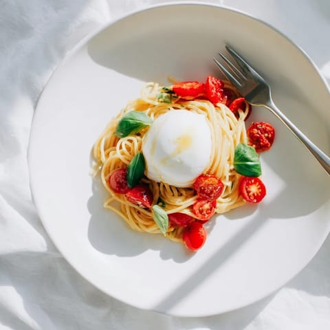 Freshly cooked Burrata Caprese Pasta with juicy cherry tomatoes and melted burrata on a white plate.